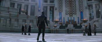Movie still from “The Hunger Games: Mockingjay - Part 2” (2015), directed by Francis Lawrence – A man in a black outfit standing in front of a building; Wide shot, Low angle