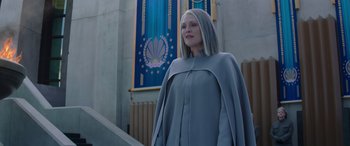 Movie still from “The Hunger Games: Mockingjay - Part 2” (2015), directed by Francis Lawrence – A woman in a blue dress standing in front of a flag; Medium shot, Low angle