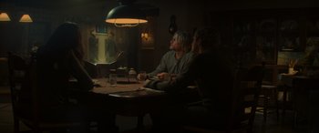Movie still from “The Hunger Games: Mockingjay - Part 2” (2015), directed by Francis Lawrence – Two people sitting at a table in a dimly - lit room; Wide shot, Over the shoulder angle