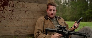 Movie still from “The Hunt” (2020), directed by Craig Zobel – A man holding a gun with blood on his face; Medium shot, Over the shoulder angle