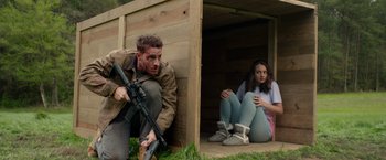 Movie still from “The Hunt” (2020), directed by Craig Zobel – A man and a woman sitting on the ground with a rifle; Medium shot, High angle