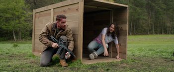 Movie still from “The Hunt” (2020), directed by Craig Zobel – A man and a woman are crouched down in a wooden hut; Medium shot, High angle