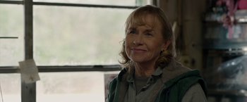 Movie still from “The Hunt” (2020), directed by Craig Zobel – An older woman smiling at the camera in front of a window; Close Up shot, Over the shoulder angle