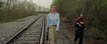 Movie still from “The Hunt” (2020), directed by Craig Zobel – A woman standing next to train tracks in a wooded area; Medium shot, Low angle