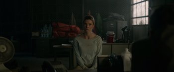 Movie still from “The Hunt” (2020), directed by Craig Zobel – A woman standing in front of a table in a cluttered room; Medium shot, Over the shoulder angle
