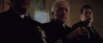 Movie still from “The Hunt for Red October” (1990), directed by John McTiernan – An older man in a suit and tie holding a guitar; Close Up shot, Over the shoulder angle