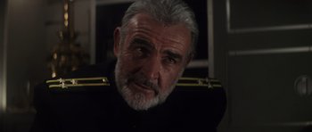 Movie still from “The Hunt for Red October” (1990), directed by John McTiernan – An older man wearing a black uniform looking at the camera; Close Up shot, Over the shoulder angle