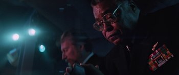 Movie still from “The Hunt for Red October” (1990), directed by John McTiernan – A man in a suit and glasses looking at his cell phone; Close Up shot, Low angle