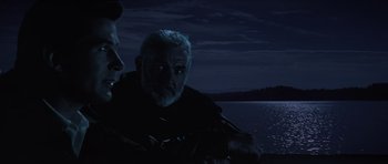 Movie still from “The Hunt for Red October” (1990), directed by John McTiernan – A man sitting next to another man on a boat at night; Close Up shot, Over the shoulder angle