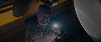 Movie still from “The Ice Road” (2021), directed by Jonathan Hensleigh – A bald man holding a flashlight in a dark room; Close Up shot, Overhead angle