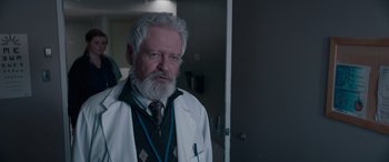 Movie still from “The Ice Road” (2021), directed by Jonathan Hensleigh – An older man in a white lab coat and tie; Close Up shot, Over the shoulder angle