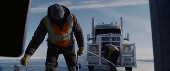 Movie still from “The Ice Road” (2021), directed by Jonathan Hensleigh – Two men working on a large semi truck; Wide shot, Low angle