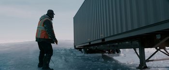 Movie still from “The Ice Road” (2021), directed by Jonathan Hensleigh – A man standing in the snow next to a trailer; Wide shot, Low angle