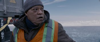 Movie still from “The Ice Road” (2021), directed by Jonathan Hensleigh – A man wearing an orange and gray vest and a hat; Close Up shot, Low angle