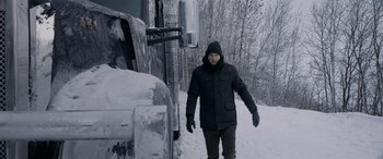 Movie still from “The Ice Road” (2021), directed by Jonathan Hensleigh – A man walking in the snow next to a large truck; Wide shot, Over the shoulder angle