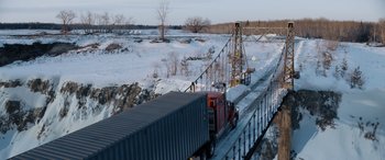 Movie still from “The Ice Road” (2021), directed by Jonathan Hensleigh – A large semi truck driving on a bridge over a snow covered river; Extreme Wide shot, High angle