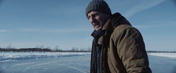 Movie still from “The Ice Road” (2021), directed by Jonathan Hensleigh – A man in a winter coat and a hat standing in the middle of a field; Medium shot, Over the shoulder angle