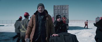 Movie still from “The Ice Road” (2021), directed by Jonathan Hensleigh – A man standing next to another man holding a piece of luggage; Medium shot, Low angle