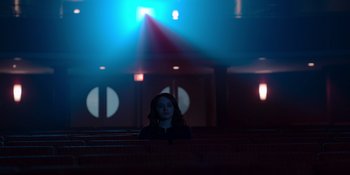 Movie still from “The In Between” (2022), directed by Arie Posin – A woman is sitting in a dark room; Extreme Wide shot, Low angle