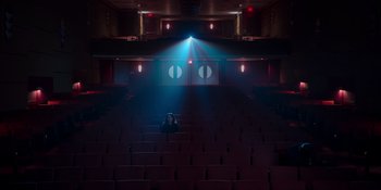 Movie still from “The In Between” (2022), directed by Arie Posin – A person sitting in the middle of an empty theater; Extreme Wide shot, High angle