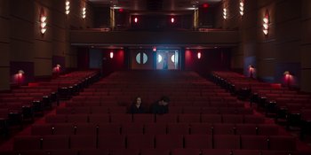 Movie still from “The In Between” (2022), directed by Arie Posin – Two people are sitting in a theater with red seats; Extreme Wide shot, High angle