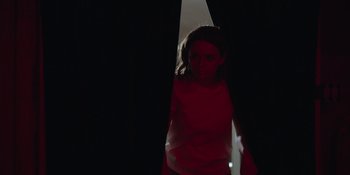 Movie still from “The In Between” (2022), directed by Arie Posin – A woman standing in a dark room looking at the camera; Medium shot, Low angle