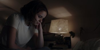 Movie still from “The In Between” (2022), directed by Arie Posin – A woman sitting in front of a laptop computer in a dark room; Close Up shot, Low angle