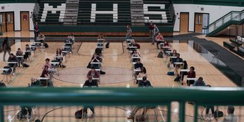 Movie still from “The In Between” (2022), directed by Arie Posin – A group of people sitting on top of a basketball court; Extreme Wide shot, High angle