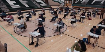 Movie still from “The In Between” (2022), directed by Arie Posin – A group of people sitting at desks in a gymnasium; Wide shot, High angle