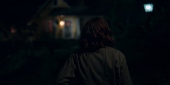 Movie still from “The In Between” (2022), directed by Arie Posin – A woman is standing in the dark looking at a house; Medium shot, Over the shoulder angle