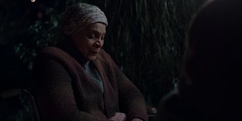 Movie still from “The In Between” (2022), directed by Arie Posin – An older woman sitting in front of some trees; Close Up shot, Over the shoulder angle