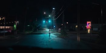 Movie still from “The In Between” (2022), directed by Arie Posin – A person standing on the side of a road at night; Extreme Wide shot, High angle