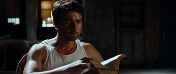 Movie still from “The Incredible Hulk” (2008), directed by Louis Leterrier – A man in a white tank top holding a book; Close Up shot, Low angle