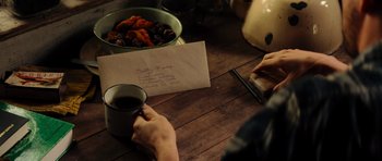 Movie still from “The Incredible Hulk” (2008), directed by Louis Leterrier – A person holding a cup of coffee at a wooden table; Extreme Close Up shot, High angle
