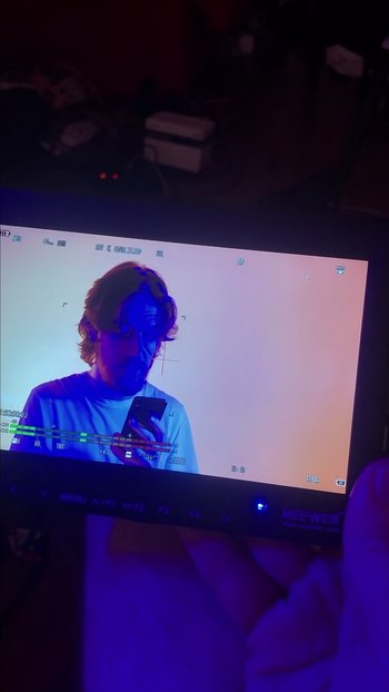 Movie still from “The Inside Outtakes” (2022), directed by Bo Burnham – A man is looking at his cell phone on a television screen; Extreme Close Up shot, Over the shoulder angle