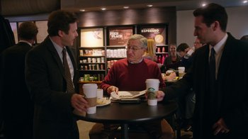 Movie still from “The Intern” (2015), directed by Nancy Meyers – A man and a woman sitting at a table with cups of coffee; Medium shot, Over the shoulder angle