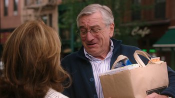Movie still from “The Intern” (2015), directed by Nancy Meyers – An older man is holding a bag and talking to an older woman; Medium shot, Over the shoulder angle