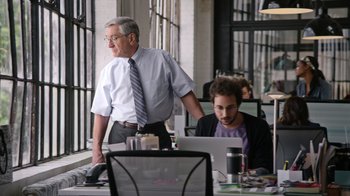 Movie still from “The Intern” (2015), directed by Nancy Meyers – A man standing in front of a laptop computer in front of another man; Medium shot, Over the shoulder angle