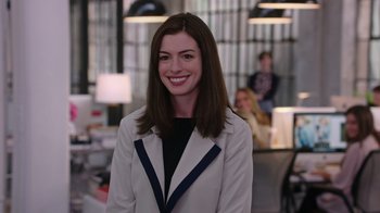 Movie still from “The Intern” (2015), directed by Nancy Meyers – A woman in a white jacket smiling for the camera; Medium shot, Over the shoulder angle