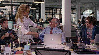 Movie still from “The Intern” (2015), directed by Nancy Meyers – An older man sitting at a desk with a woman; Medium shot, Over the shoulder angle