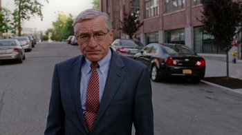 Movie still from “The Intern” (2015), directed by Nancy Meyers – An older man wearing a suit and tie standing on the side of the street; Close Up shot, Over the shoulder angle