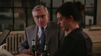 Movie still from “The Intern” (2015), directed by Nancy Meyers – An older man and a young woman are drinking beer together; Medium shot, Over the shoulder angle