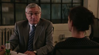Movie still from “The Intern” (2015), directed by Nancy Meyers – An older man wearing a suit and tie talking to an older woman; Medium shot, Over the shoulder angle