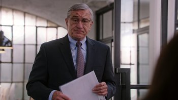 Movie still from “The Intern” (2015), directed by Nancy Meyers – An older man in a suit and tie holding a piece of paper; Medium shot, Over the shoulder angle