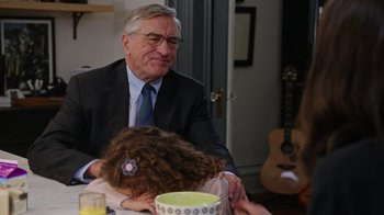 Movie still from “The Intern” (2015), directed by Nancy Meyers – An older man sitting at a table with a young girl; Medium shot, Over the shoulder angle