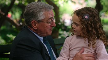 Movie still from “The Intern” (2015), directed by Nancy Meyers – An older man sitting next to a little girl; Close Up shot, Over the shoulder angle