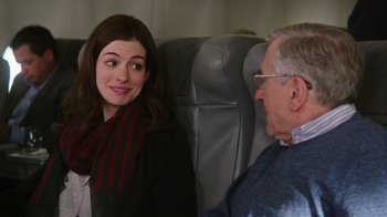 Movie still from “The Intern” (2015), directed by Nancy Meyers – An older man sitting next to a woman on a plane; Medium shot, Over the shoulder angle