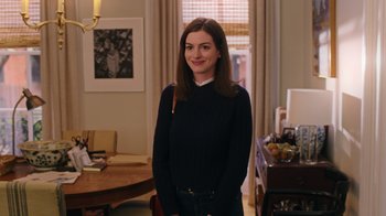 Movie still from “The Intern” (2015), directed by Nancy Meyers – A woman standing in front of a table in a living room; Medium shot, Over the shoulder angle