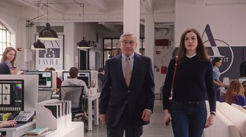 Movie still from “The Intern” (2015), directed by Nancy Meyers – A man and a woman walking in an office space; Medium shot, Over the shoulder angle
