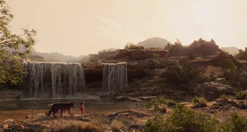 Movie still from “The Jungle Book” (2016), directed by Jon Favreau – A person standing next to a body of water near a waterfall; Extreme Wide shot, Low angle